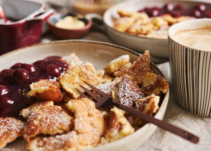 Una toma de deliciosos panqueques esponjosos con cereza y azúcar en polvo. A selective focus closeup shot of delicious fluffy pancakes with cherry and powdered sugar and a cup of coffee on the table